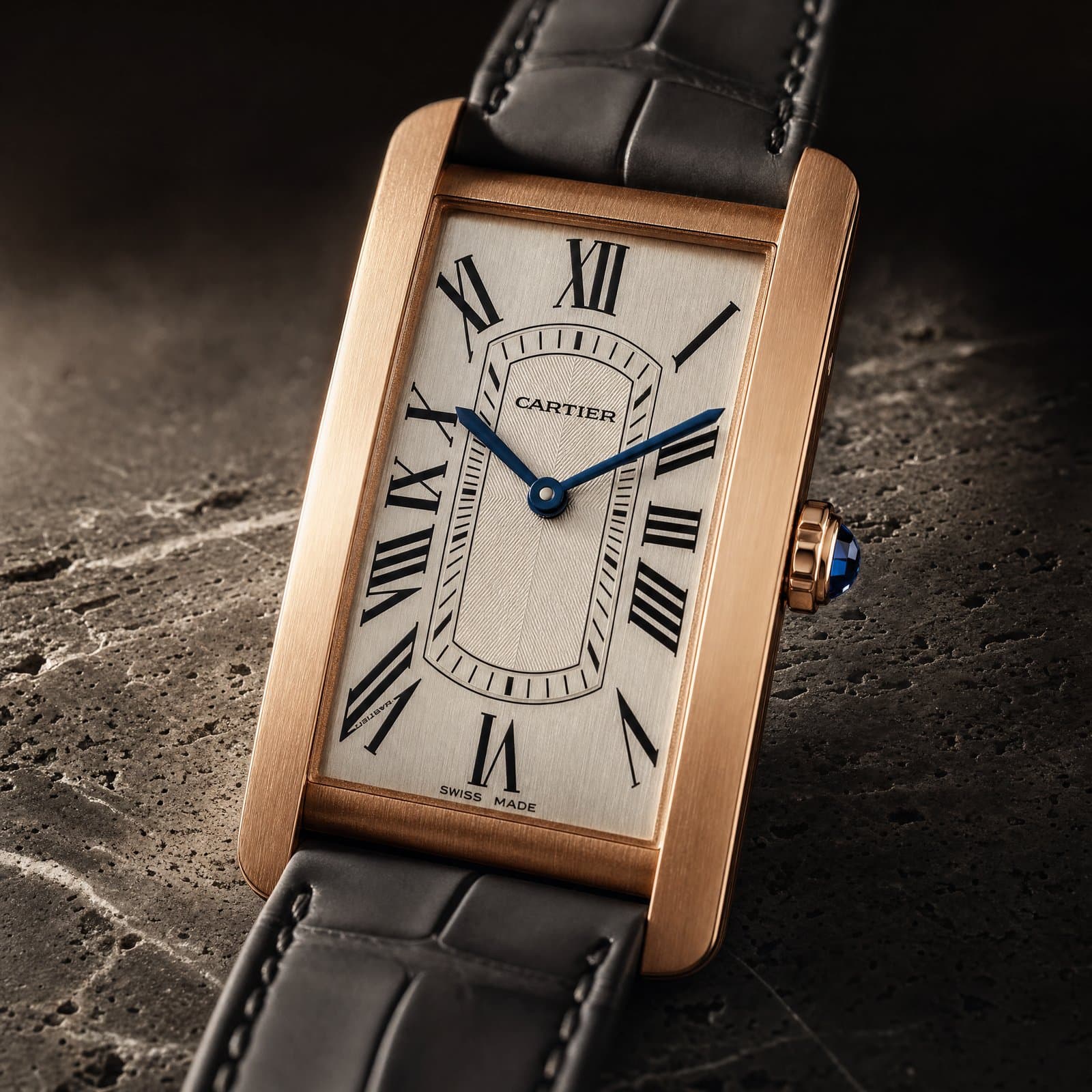 Macro of a rose-gold Cartier Tank on dark travertine