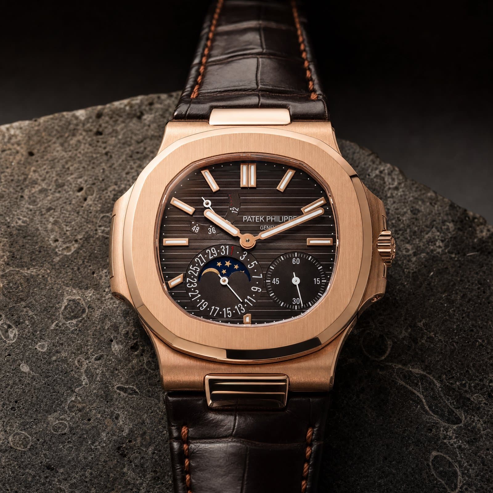 Macro of a rose-gold Nautilus moonphase dial on dark travertine