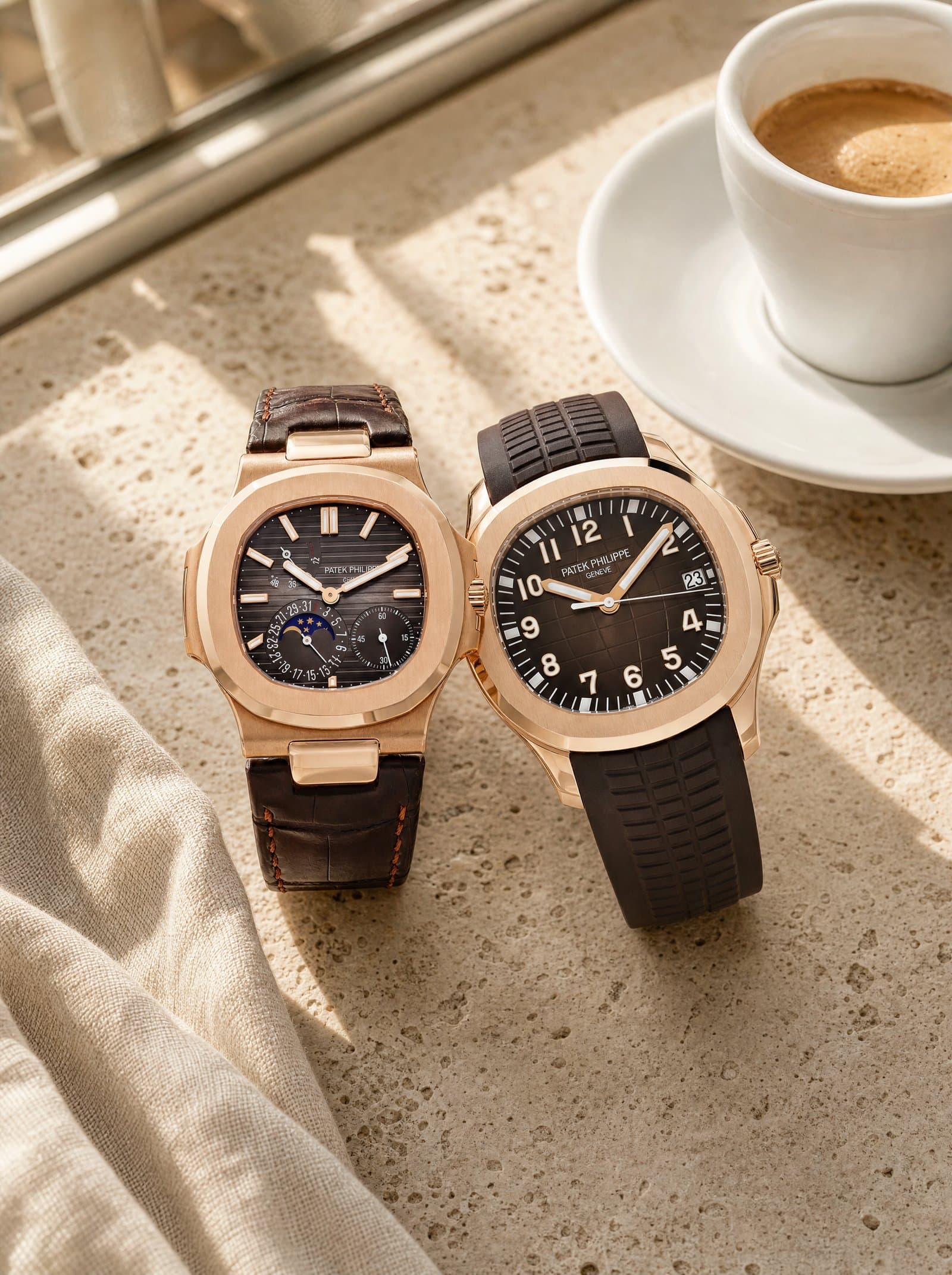 A rose-gold Nautilus and an Aquanaut resting together on a travertine café table beside an espresso